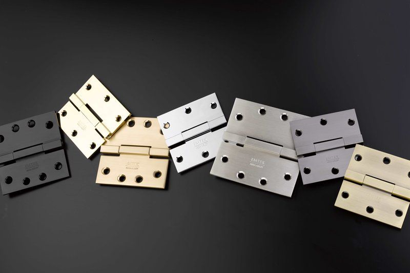 Various Emtek hinges in different finishes on a black background, including both residential and heavy duty hinges from Emtek.